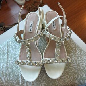 Miu Miu white sandals with thick heel and rhinestone details.